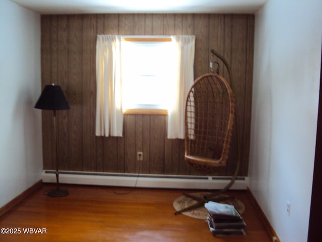 spare room featuring a baseboard radiator, wood-type flooring, and wood walls