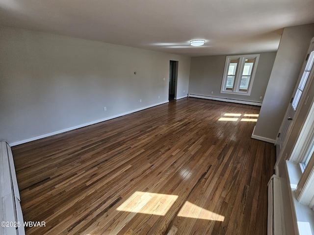 spare room featuring baseboards, baseboard heating, and dark wood-style floors