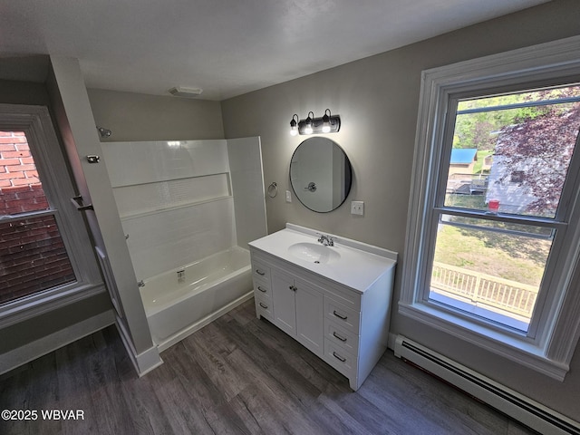 bathroom featuring vanity, washtub / shower combination, wood finished floors, and baseboard heating