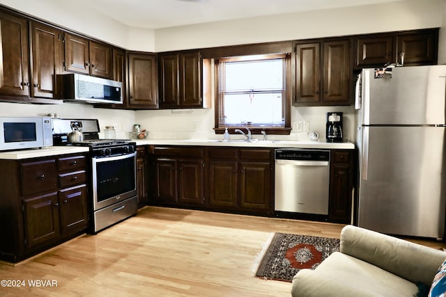 kitchen with dark brown cabinetry, sink, stainless steel appliances, and light hardwood / wood-style floors