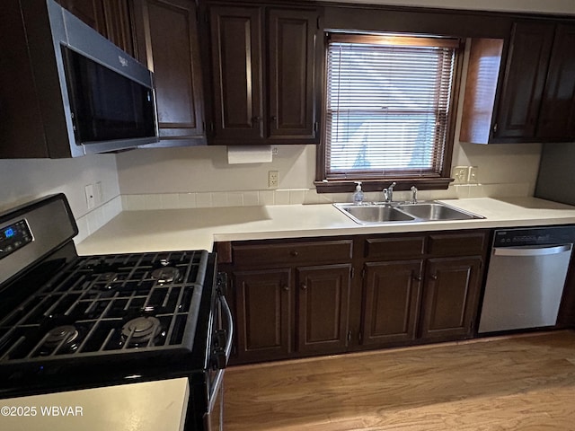 kitchen featuring appliances with stainless steel finishes, sink, dark brown cabinets, and light hardwood / wood-style flooring