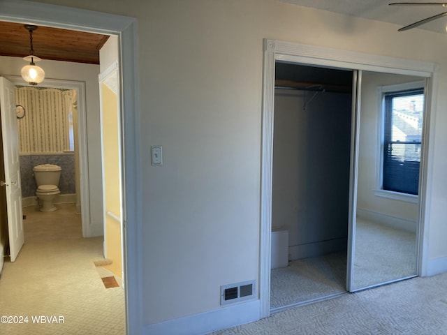 unfurnished bedroom featuring light colored carpet, ensuite bath, a closet, and ceiling fan