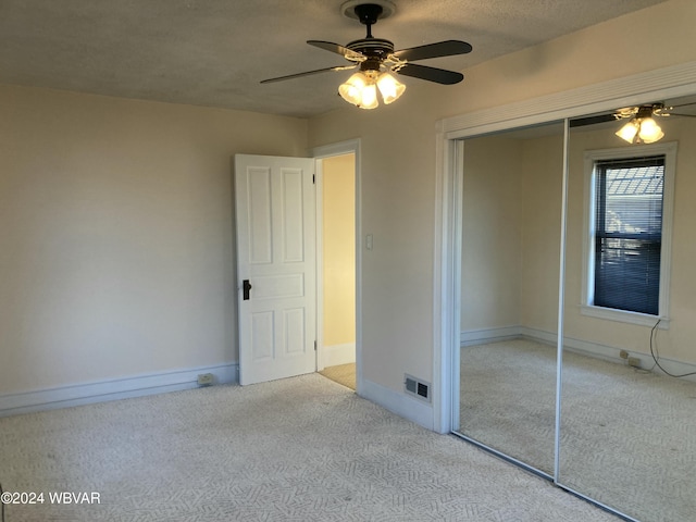 unfurnished bedroom featuring ceiling fan, a closet, light colored carpet, and a textured ceiling