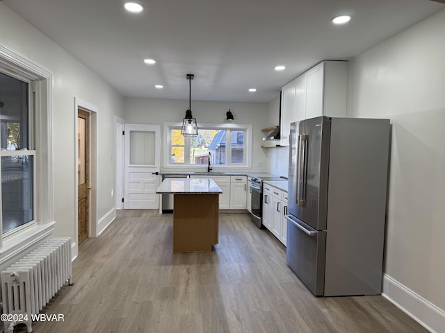 kitchen with appliances with stainless steel finishes, a kitchen island, decorative light fixtures, radiator heating unit, and white cabinetry