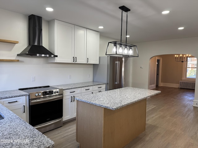 kitchen featuring wall chimney range hood, radiator heating unit, a kitchen island, white cabinetry, and stainless steel appliances