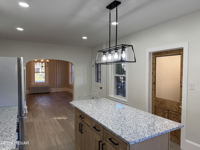 kitchen with light stone countertops, radiator heating unit, dark wood-type flooring, stainless steel fridge, and pendant lighting