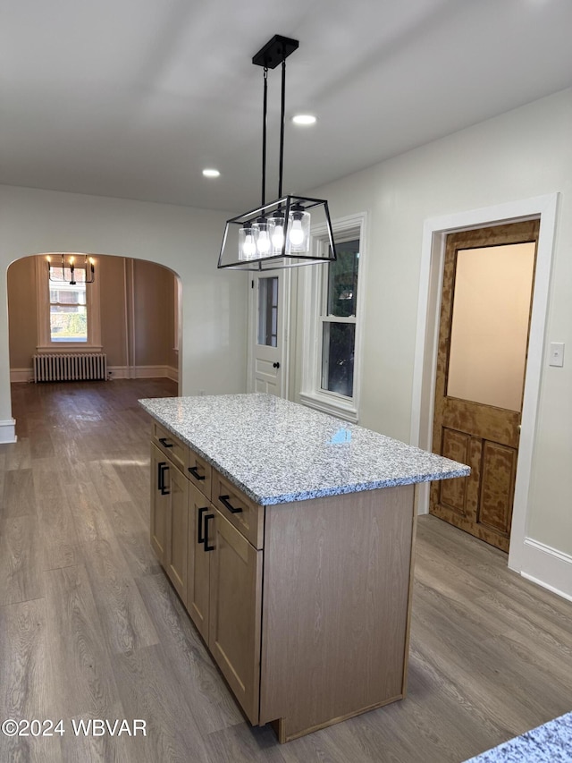 kitchen with radiator heating unit, a center island, hanging light fixtures, and light hardwood / wood-style flooring