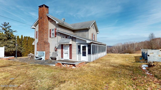 view of side of property with a sunroom, a chimney, and a lawn