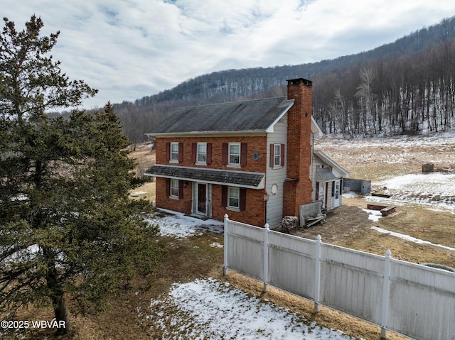 exterior space with brick siding, a chimney, fence, a mountain view, and a forest view