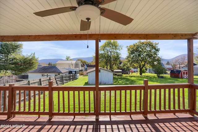 wooden terrace featuring a mountain view, ceiling fan, a storage unit, and a lawn