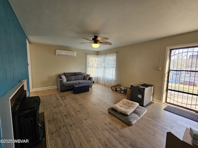 living room with a ceiling fan, an AC wall unit, wood finished floors, and baseboards