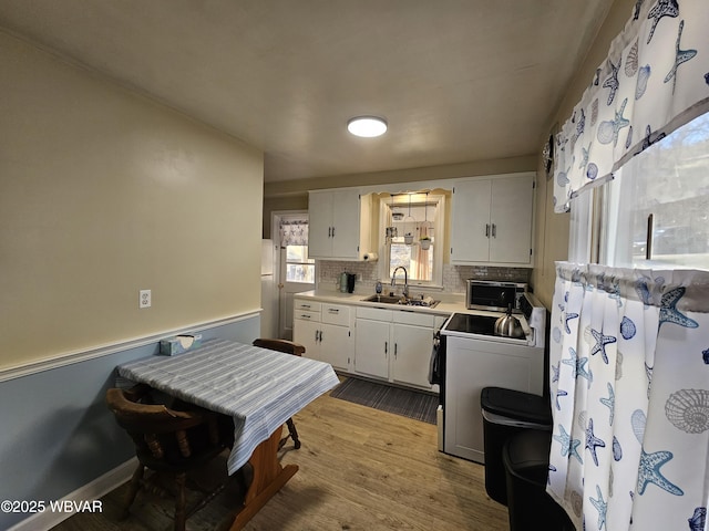 kitchen with a sink, stainless steel microwave, wood finished floors, white cabinets, and range