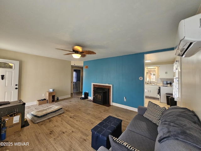 living area with a wall mounted air conditioner, light wood finished floors, baseboards, ceiling fan, and a wood stove