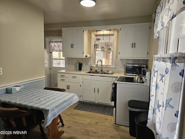 kitchen with white cabinets, range, light wood-type flooring, and a sink