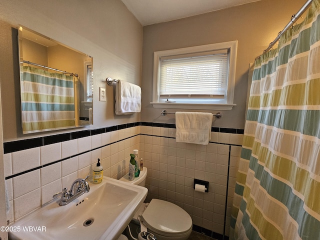 bathroom featuring a sink, toilet, tile walls, and wainscoting