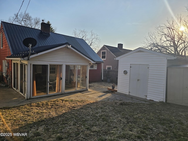 rear view of house featuring an outbuilding, fence, a storage shed, metal roof, and a chimney