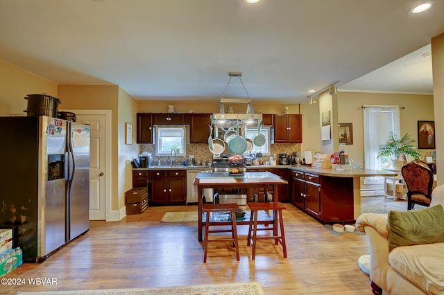 kitchen featuring stainless steel appliances, decorative backsplash, sink, hanging light fixtures, and light hardwood / wood-style flooring