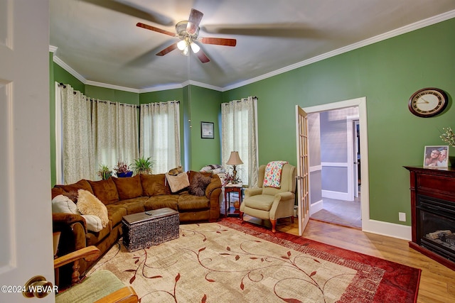 living area featuring baseboards, ceiling fan, wood finished floors, crown molding, and a fireplace