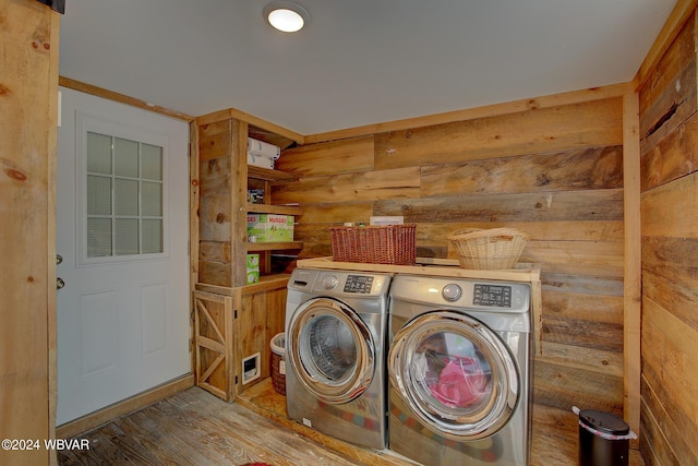 clothes washing area with laundry area, independent washer and dryer, wood finished floors, and wooden walls