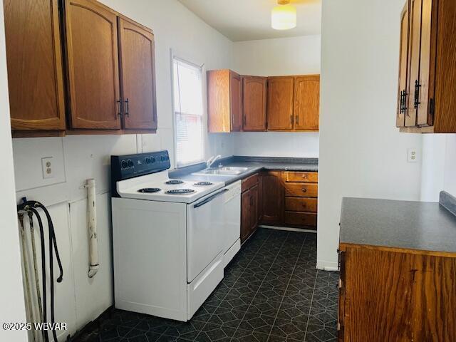 kitchen with white appliances, dark countertops, dark floors, brown cabinets, and a sink