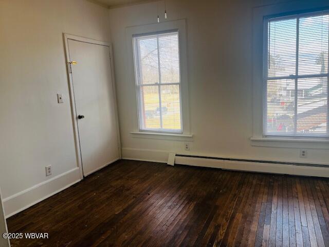 unfurnished room with a baseboard heating unit, dark wood-type flooring, and baseboards