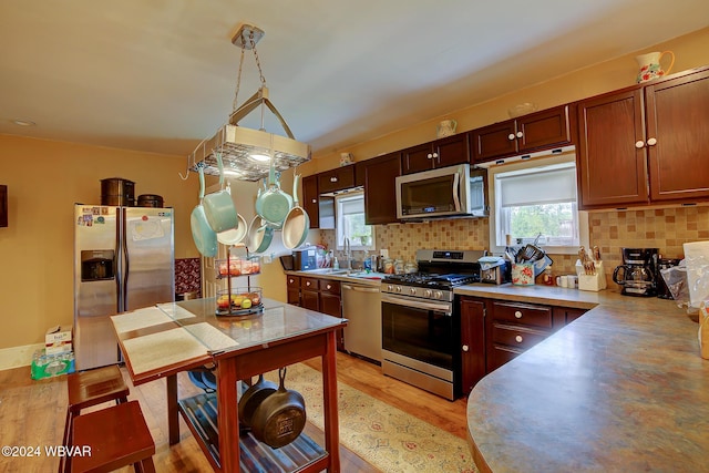 kitchen featuring stainless steel appliances, decorative backsplash, pendant lighting, light hardwood / wood-style flooring, and sink