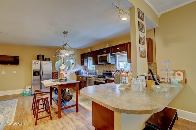 kitchen with tasteful backsplash, light hardwood / wood-style floors, kitchen peninsula, hanging light fixtures, and stainless steel appliances