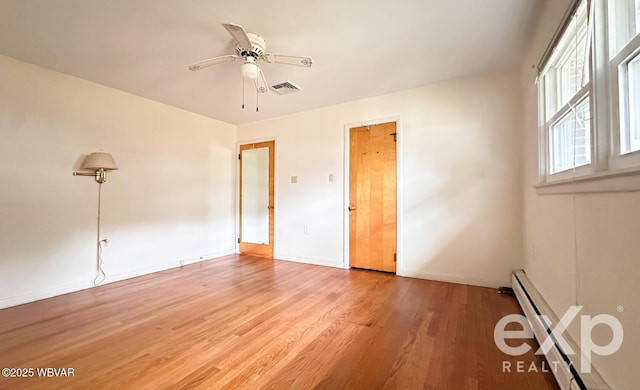 empty room featuring light wood finished floors, visible vents, a baseboard heating unit, ceiling fan, and baseboards