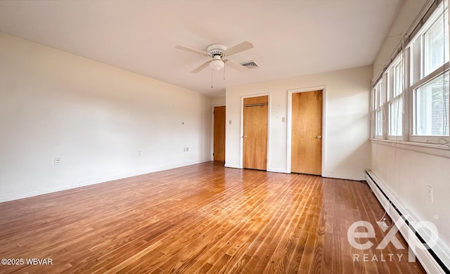 unfurnished bedroom featuring a baseboard heating unit, two closets, baseboards, and wood finished floors