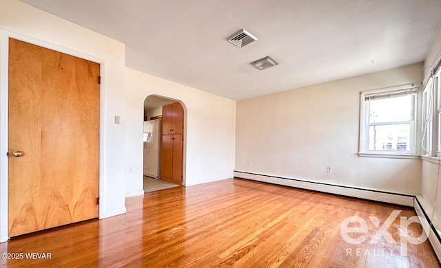 unfurnished room featuring baseboard heating, visible vents, arched walkways, and wood finished floors