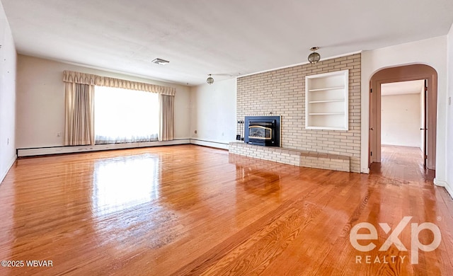 unfurnished living room featuring arched walkways, built in shelves, a baseboard heating unit, wood finished floors, and visible vents