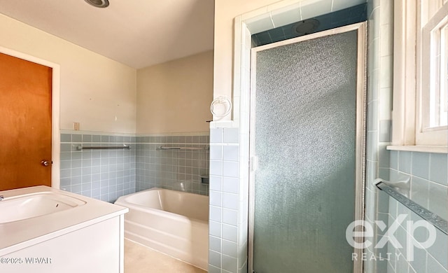 bathroom featuring vanity, tile walls, wainscoting, a bath, and a stall shower