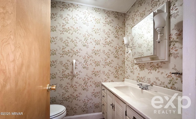 half bathroom featuring toilet, wallpapered walls, baseboards, and vanity