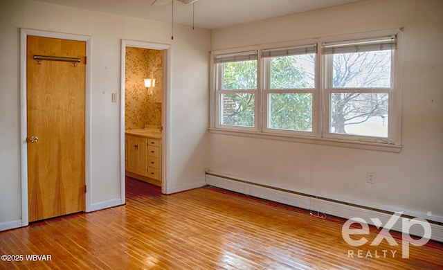 unfurnished bedroom featuring a baseboard heating unit, baseboards, connected bathroom, and light wood finished floors