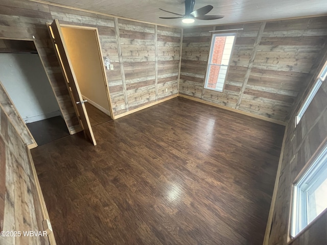 empty room featuring a healthy amount of sunlight, wood walls, ceiling fan, and dark wood-type flooring