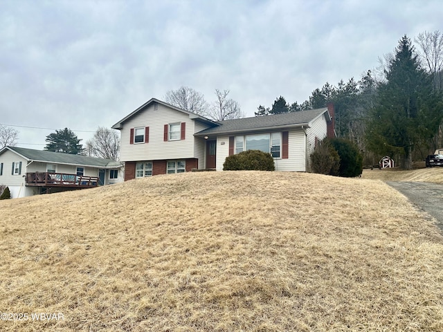 tri-level home with brick siding, a chimney, and a front lawn