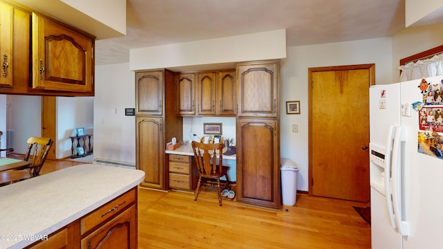 kitchen with light countertops, light wood-style flooring, white fridge with ice dispenser, brown cabinetry, and built in study area