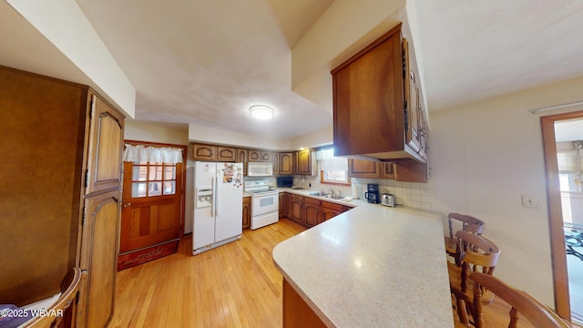 kitchen featuring light wood-type flooring, a sink, white appliances, a peninsula, and decorative backsplash