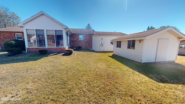 back of house featuring an outbuilding, a lawn, brick siding, and a sunroom