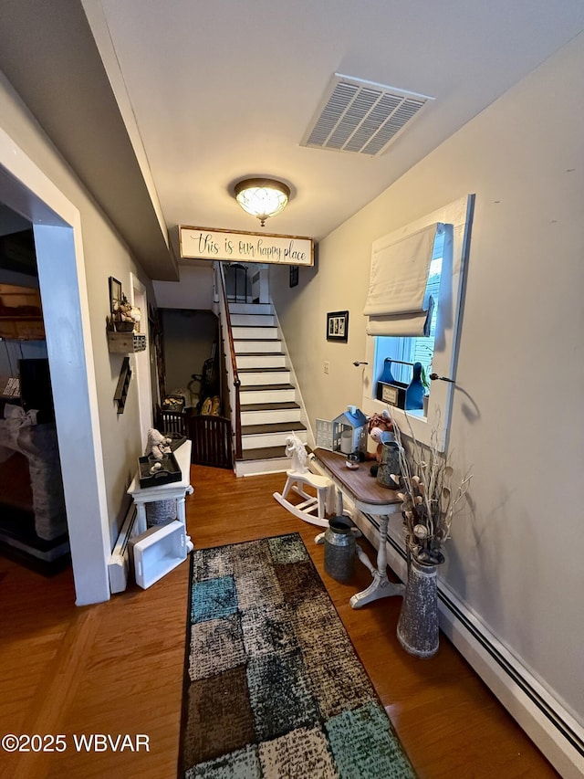 corridor with stairway, a baseboard radiator, wood finished floors, and visible vents