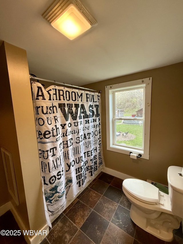 bathroom with a shower with shower curtain, stone tile floors, toilet, and baseboards
