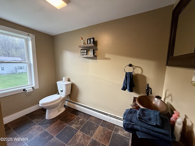half bathroom with baseboards, stone tile floors, toilet, and baseboard heating