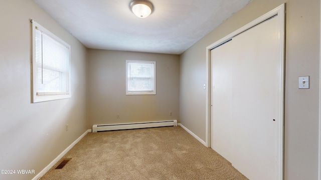 unfurnished bedroom featuring a closet, light colored carpet, and a baseboard heating unit