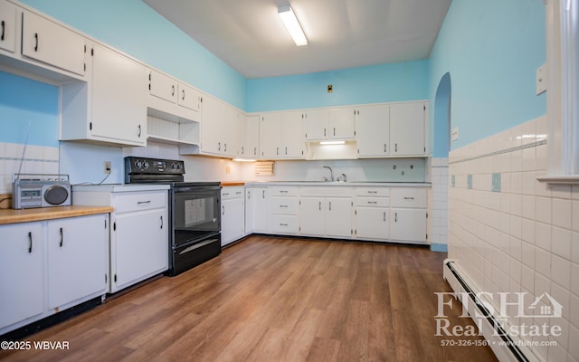 kitchen featuring hardwood / wood-style floors, a baseboard radiator, black electric range oven, white cabinets, and sink