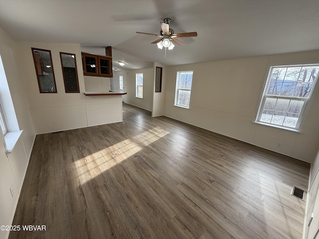 unfurnished living room featuring dark hardwood / wood-style flooring, vaulted ceiling, a wealth of natural light, and ceiling fan