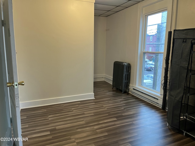 empty room featuring a drop ceiling, radiator heating unit, dark wood-type flooring, and baseboard heating