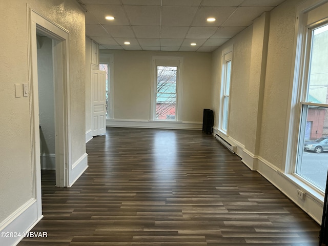 unfurnished room featuring dark hardwood / wood-style flooring, a baseboard radiator, and a drop ceiling