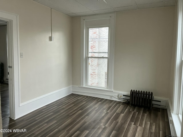 spare room featuring a drop ceiling, radiator heating unit, dark wood-type flooring, and a baseboard radiator