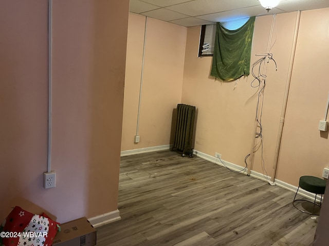 basement featuring a paneled ceiling, radiator heating unit, and wood-type flooring