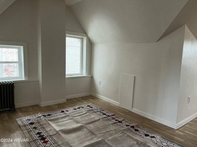 additional living space featuring radiator heating unit, wood-type flooring, and vaulted ceiling